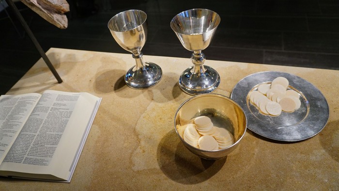 Zwei Kelche und eine Schale mit Hostien auf einem Tisch, daneben eine aufgeschlagene Bibel