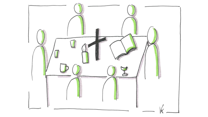 Eine Gruppe von Menschen sitzt um einen Tisch mit Kaffee, Kerze, Kreuz und Buch.