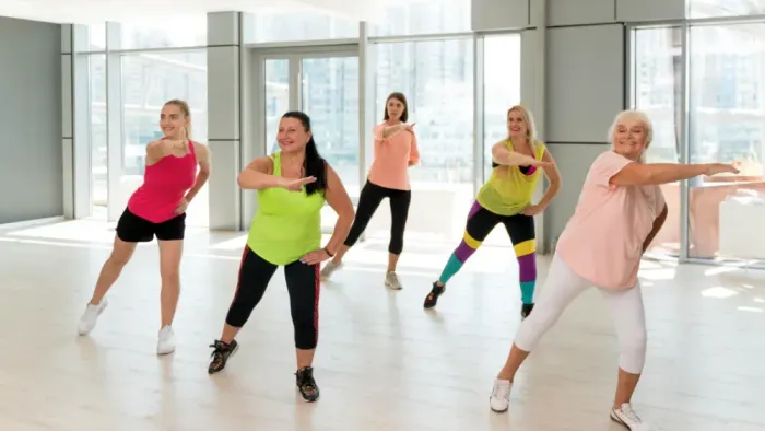 Fünf Frauen führen Tanztritte in einem Studio mit großen Fenstern aus.