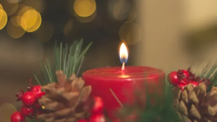 Weihnachtliche Dekoration mit brennender Kerze, Tannenzapfen und Beeren.