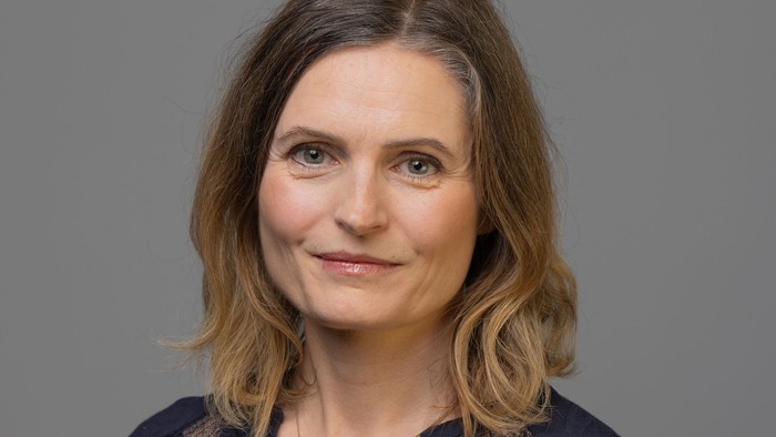 Professionelt portræt af en kvinde med skulderlangt hår iført en mørk top og halskæde.