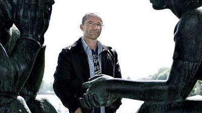 En mand står mellem to store bronzestatuer i en håndtryksstilling udendørs.