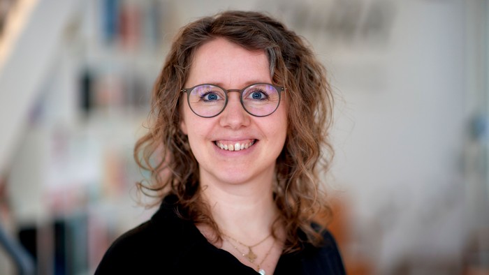 En kvinde med krøllet hår og briller smiler til kameraet.