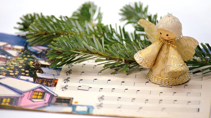 Ein goldener Engel sitzt auf Notenblättern neben einem Tannenzweig