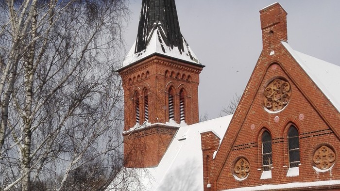 Ein rotes Backsteingebäude mit zwei Türmen, bedeckt von Schnee, vor einem klaren blauen Himmel