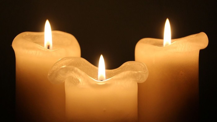 Drei brennende Kerzen in Dreiecksformation vor schwarzem Hintergrund