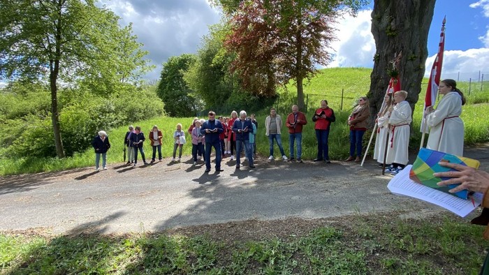 Die Gruppe versammelt sich im Freien in der Nähe eines Baumes zu einer zeremoniellen Veranstaltung mit Flaggen und Bannern.