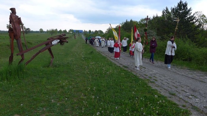 Eine Gruppe von Menschen in traditioneller Kleidung marschiert einen ländlichen Weg entlang und trägt Flaggen und Banner.