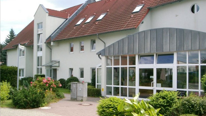 Das Bild zeigt ein modernes Gebäude mit einem großen Glasanbau und gepflegtem Garten.