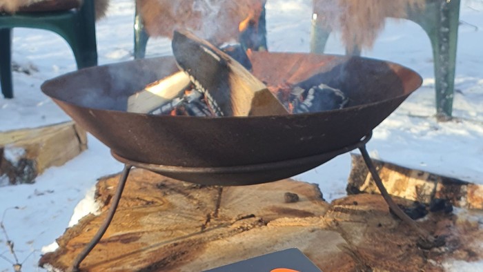 En smuk brænder i en stålbåde på en træbænke med sne omkring