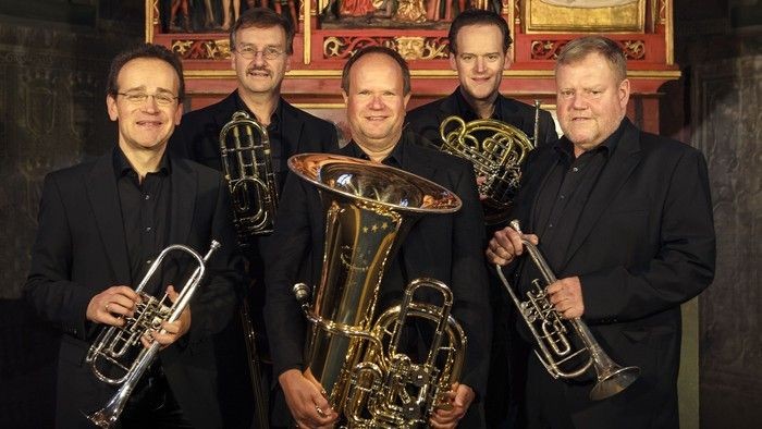 Sechs Männer mit Blechblasinstrumenten, die gemeinsam posieren.