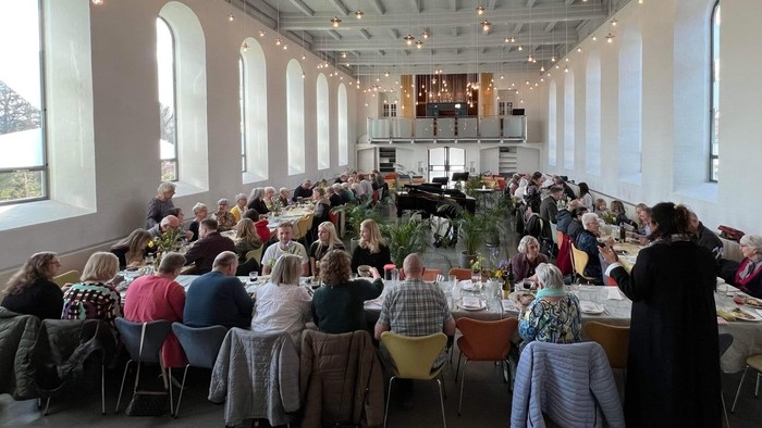 En stor sal med mange folk sidde ved lange bord og spiser.