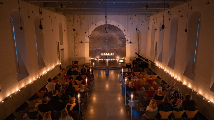 En stor hall med mange mennesker sidder på kudder og klister med lysstråler langs vægge og tak.