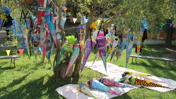 Bunte Drachen im Garten, einige auf Stangen, andere auf dem Boden