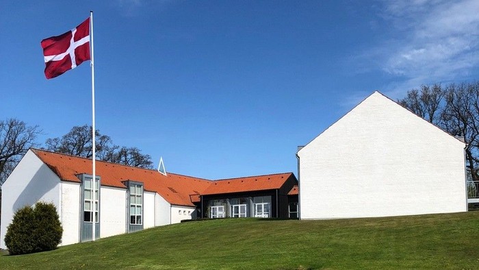 Hvid bygning med rødt tag og dansk flag på en bakke