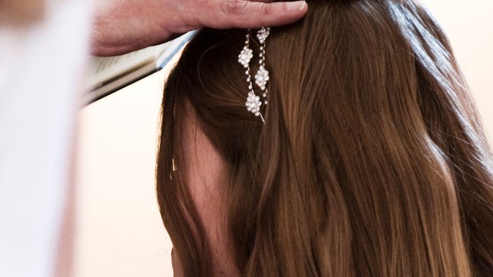 En person placerer omhyggeligt et dekorativt hårstykke i brudens opsat hår.
