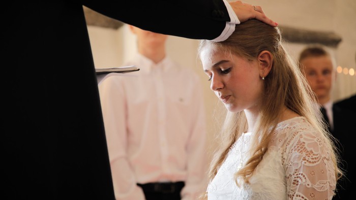En kvinde i en hvid kniplingskjole får justeret sit hår af en mand under en formel ceremoni.