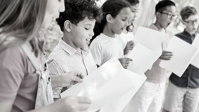 En gruppe børn og en voksen holder tomme papirer, sandsynligvis som en del af en udendørsaktivitet eller begivenhed.