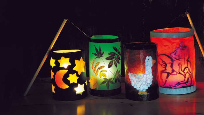 Vier leuchtende, bunte Laternen vor einem dunklen Hintergrund.