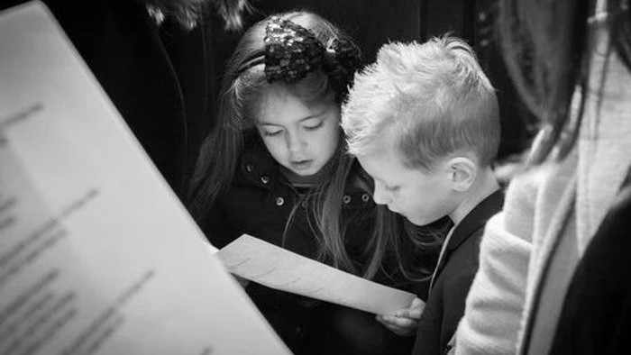 To børn studerer opmærksomt et nodehæfte sammen.