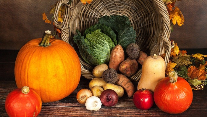 Ein Korb gefüllt mit Herbstgemüse und Kürbissen, umgeben von bunten Blättern