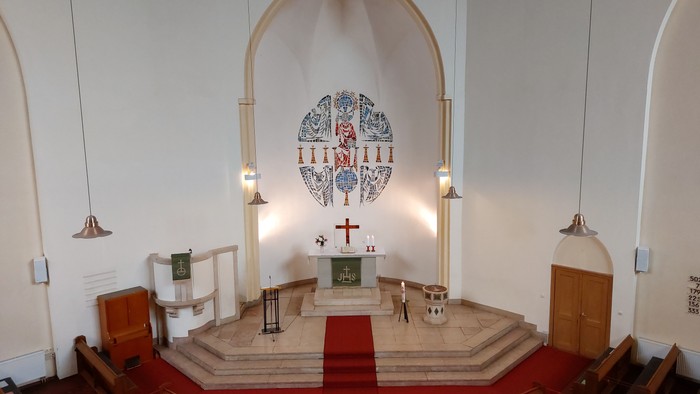 Die Kirche hat einen Altarraum mit einem großen Fenster und Holzbänken.