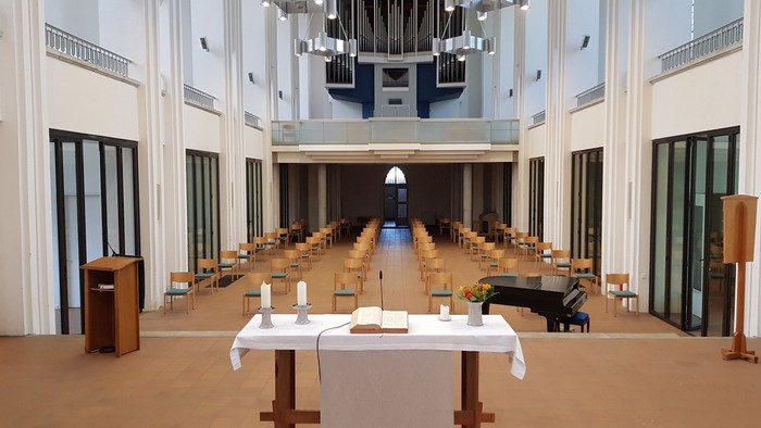 Großer Saal mit vielen Tischen und Stühlen, Podium und Deckenleuchten