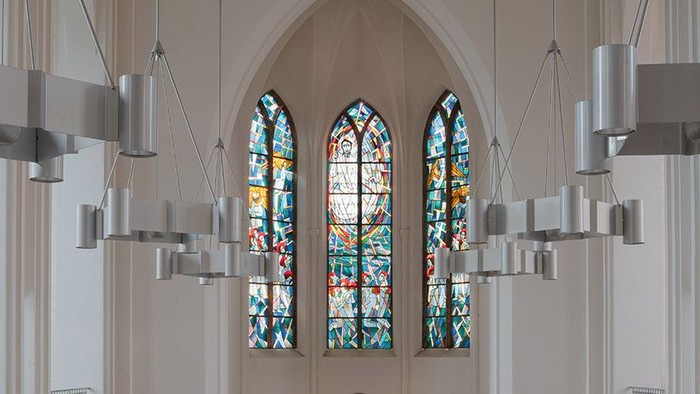 Ein Kircheninneres mit farbenfrohen Buntglasfenstern und modernen Deckenleuchten.