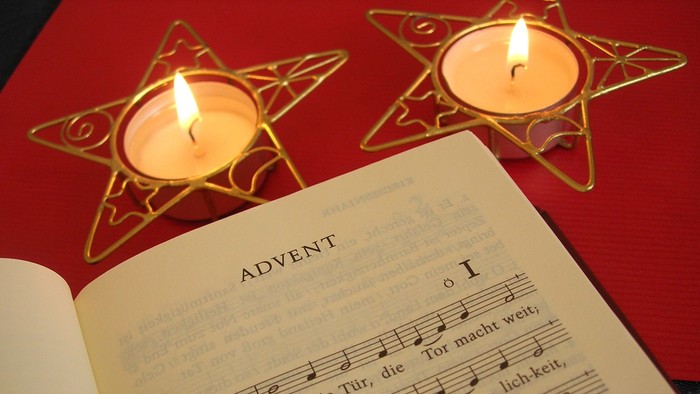 Notenblatt mit Adventslied, darüber 2 Teelichter 