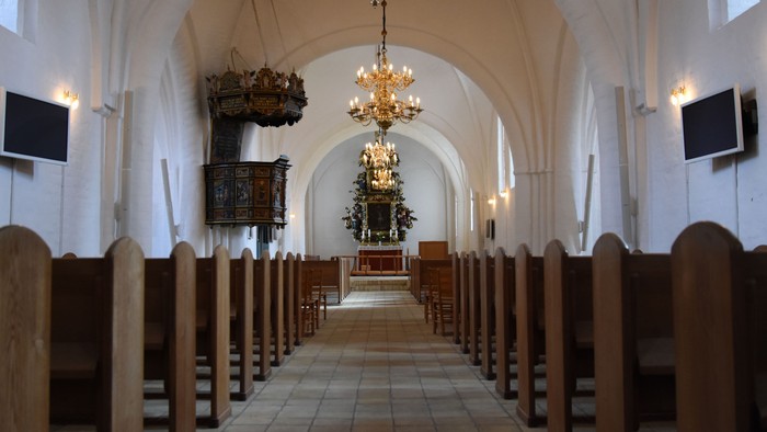 Indre del af kirke med høje vægge og belysning fra kandelier