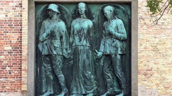 Støvletøg med tre figurer foran murstengevær