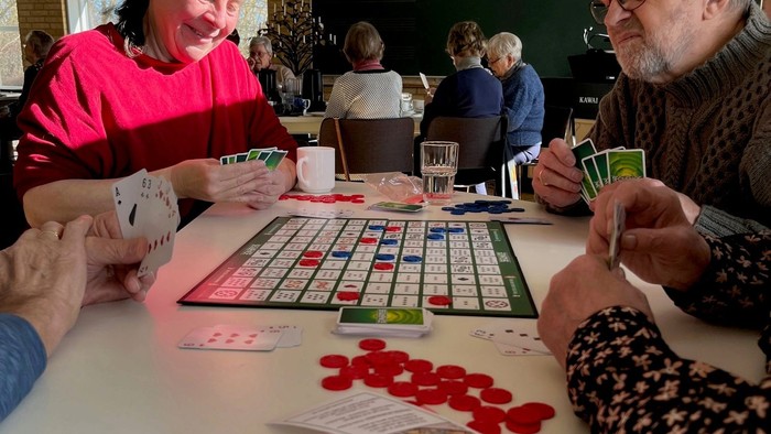 En gruppe ældre spiller Scrabble og kortspil på en bord.