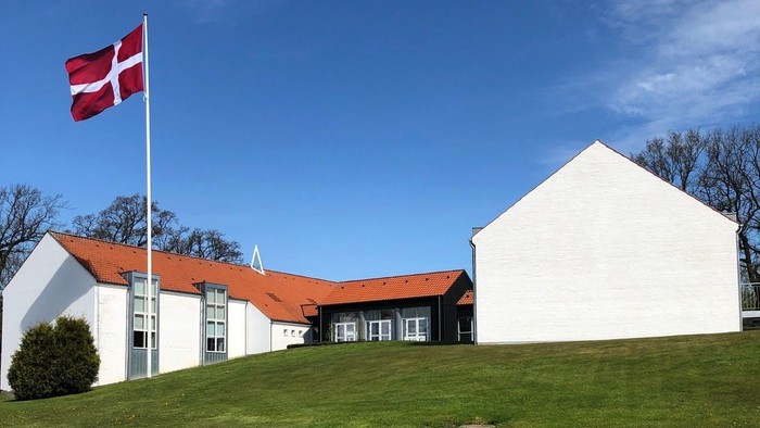 Hvidt hus med rødt tag og dansk flag på en bakke