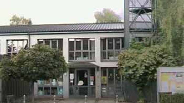 Das Bild zeigt ein modernes Gebäude mit einem hohen Turm und umgeben von Bäumen.