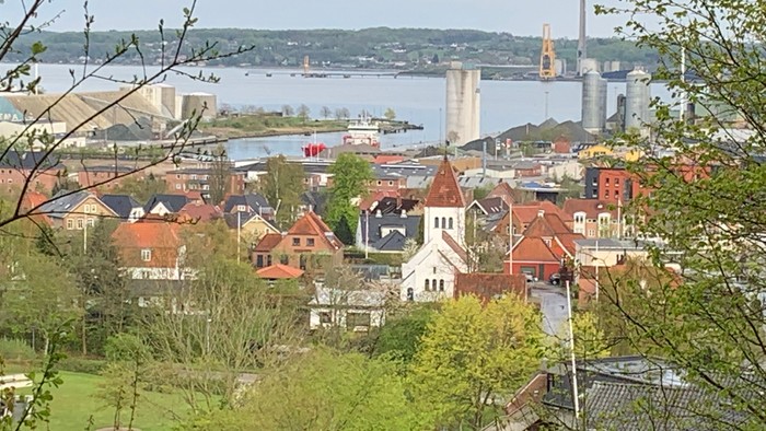 En lille by ved en flod med røde tagtegn og en kirke i midten