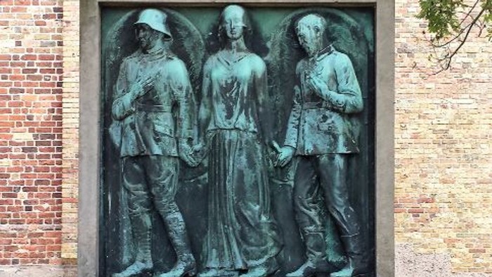 Støvletøg med tre figurer foran murstengevær