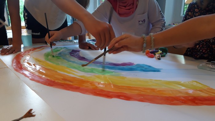 Kinder malen einen Regenbogen auf einem großen Blatt Papier
