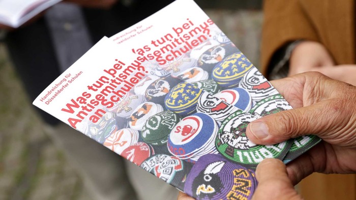 Hand hält ein Buch mit dem Titel *„Was tun bei Amtsmüsi, wenn alles schließt?“* mit bunten Illustrationen.