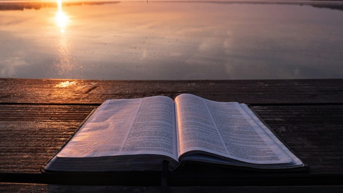 Offenes Buch liegt auf Holzsteg bei Sonnenuntergang am Wasser