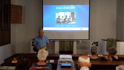 Ein Mann hält einen Vortrag vor einem Publikum, während ein Bildschirm hinter ihm zeigt