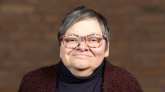 Eine Frau mit kurzem Haar und bunten Brillen lächelt.