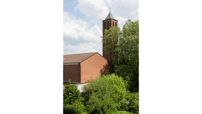 Ziegelgebäude mit hohem Turm, umgeben von Grünflächen.