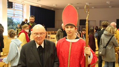 Mann im Anzug posiert mit Jungen im Kardinalkostüm.