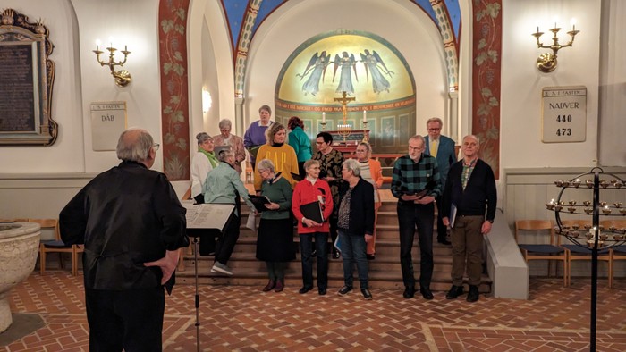 En gruppe af mennesker samles i et historisk rum med billeder og lampeskærme.