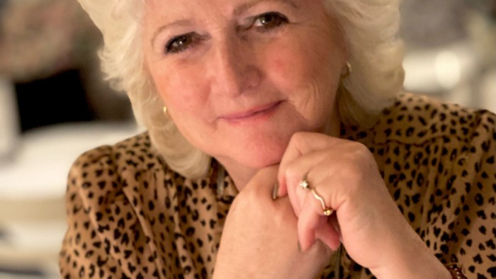 En kvinde med blondt hår i en leopardmønstret top, der poserer eftertænksomt indendørs.