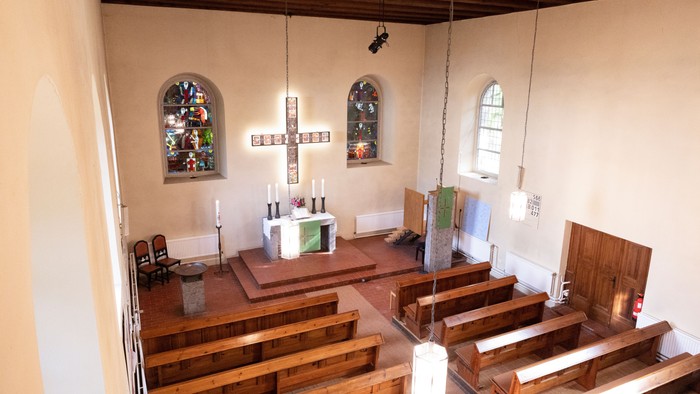 Kleine Kirche mit Holzgestühl und zwei buntverglasten Fenstern