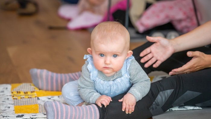 Et spæd barn sitter på gulvet og ser op med blå øjne.