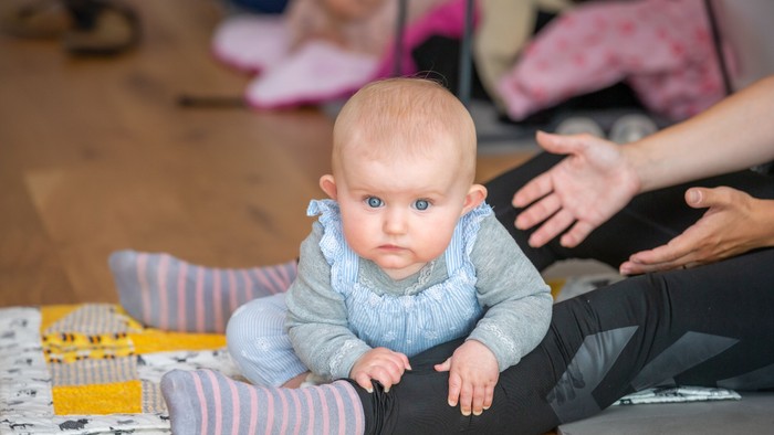 Et spæd barn sitter på gulvet og ser op med blå øjne.