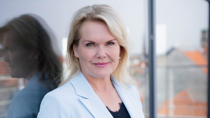 En kvinde i en hvid blazer står på en tagterrasse og smiler.