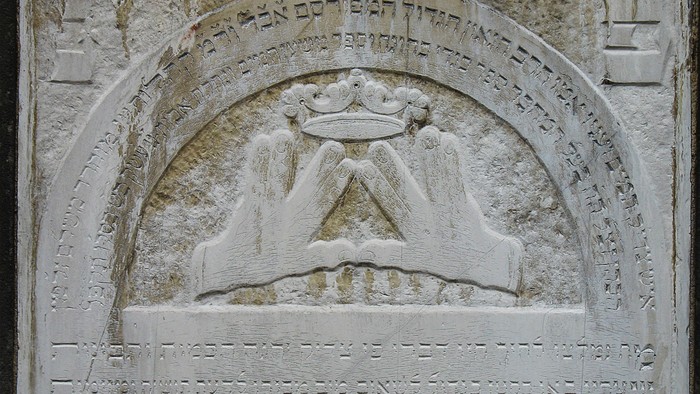 Das Bild zeigt eine steinerne Inschrift mit hebräischen Schriftzeichen und einem Symbol in der Mitte.